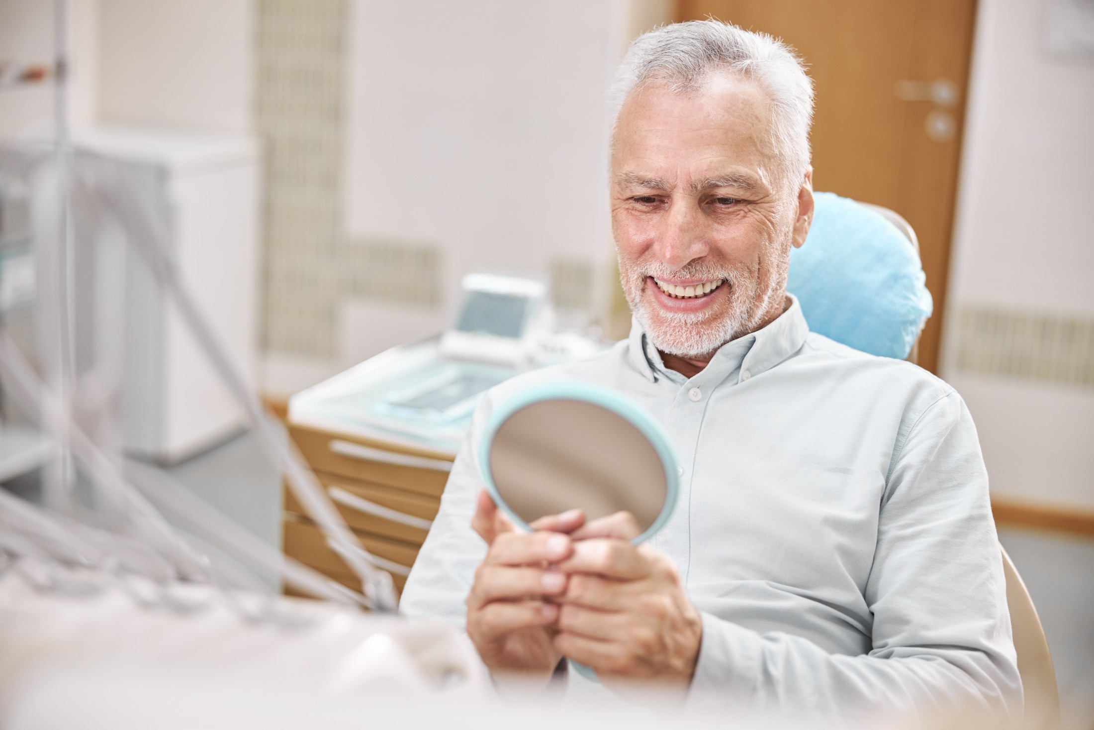 A man in a dental chair admiring his new dental implants in a hand mirror